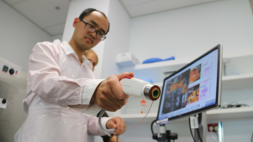 Researcher Qi Fang holds a portable imaging device in a laboratory.