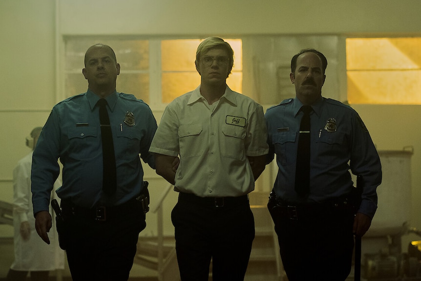 An image of a scene in the Netflix series about Jeffrey Dahmer, showing him being escorted by two policemen
