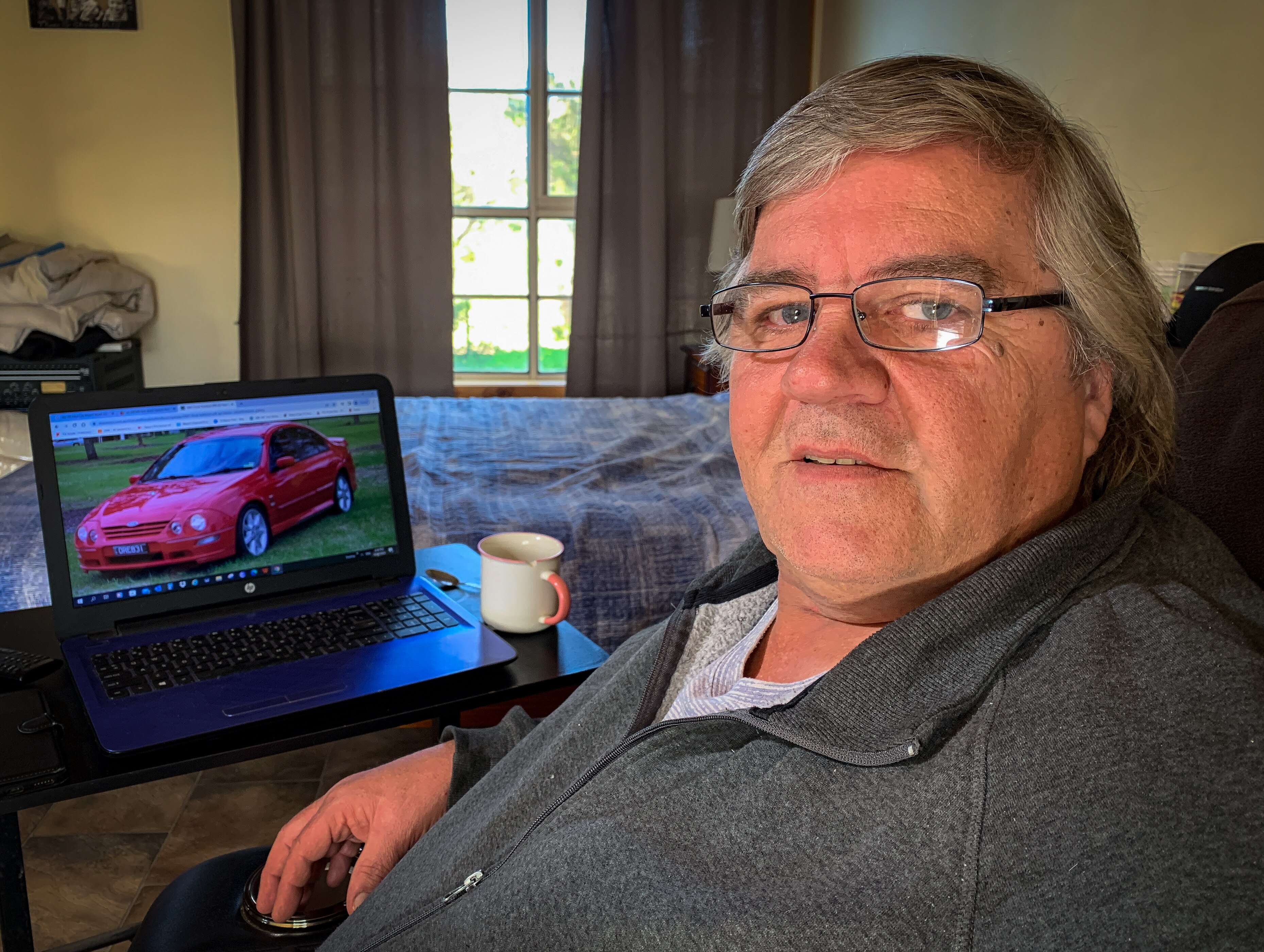 Man sitting down with a laptop in front of him showing a picture of a car.