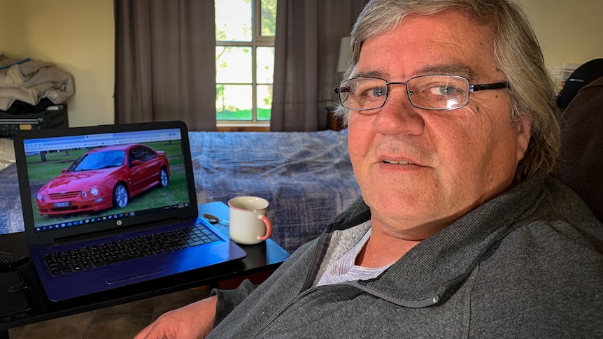 Man sitting down with a laptop in front of him showing a picture of a car.