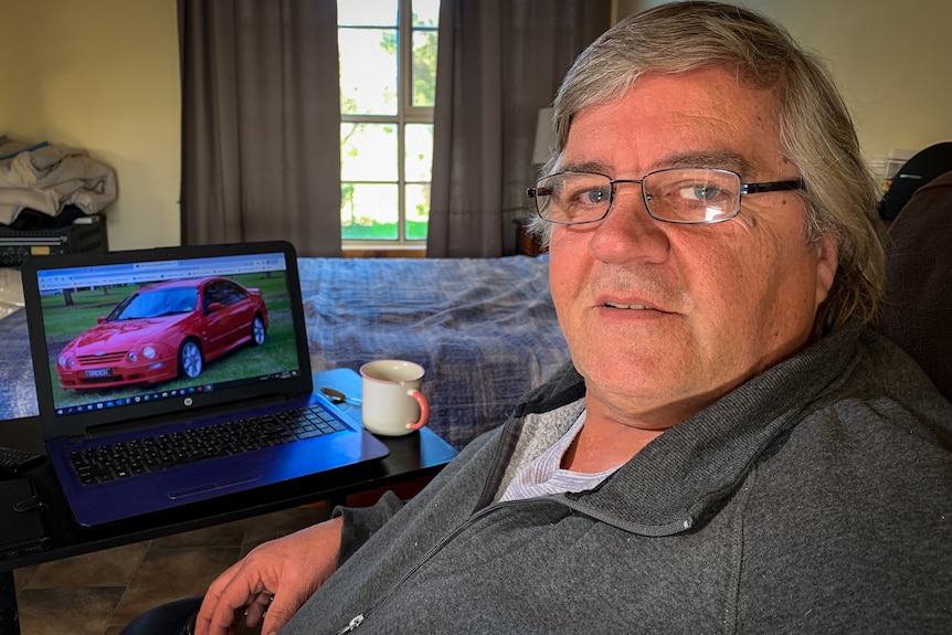 Man sitting down with a laptop in front of him showing a picture of a car.