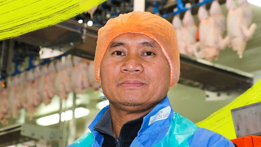 Asein ZaWaNa at chicken processing plant, with chicken carcasses hanging behind him, for a story about refugees finding work.