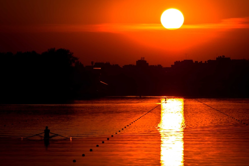 A rower on a lake as the sun sets in the background.