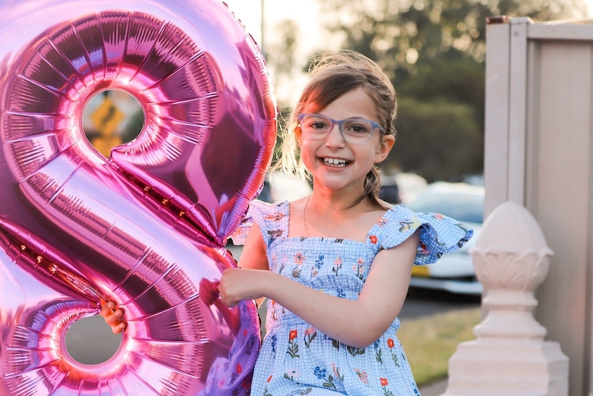 Eve Daher smiling with a balloon in the shape of the number eight.