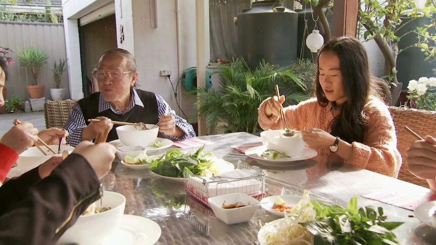 Elderly Asian man and teenage girl eat food at backyard table