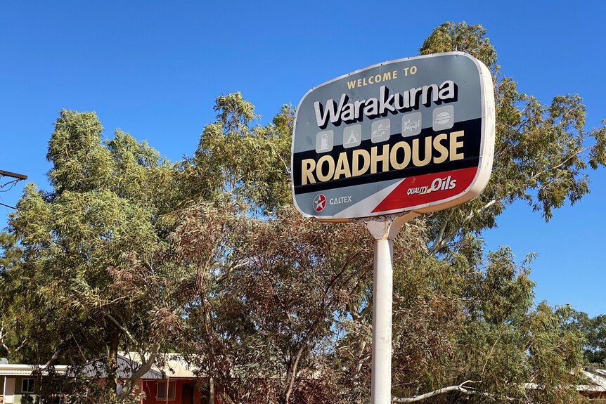 A sign that reads Warakurna road house, with trees visible behind it