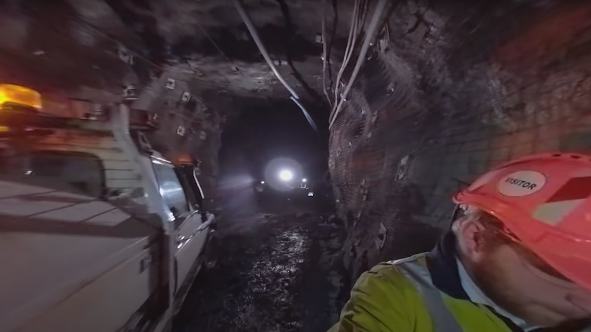 A dark tunnel with miners and vehicles driving through it.