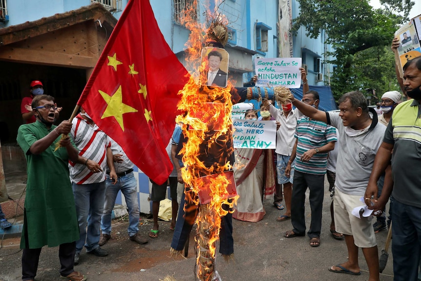 A group of Indian men hold up signs in front of a burning effigy depicting the Chinese President