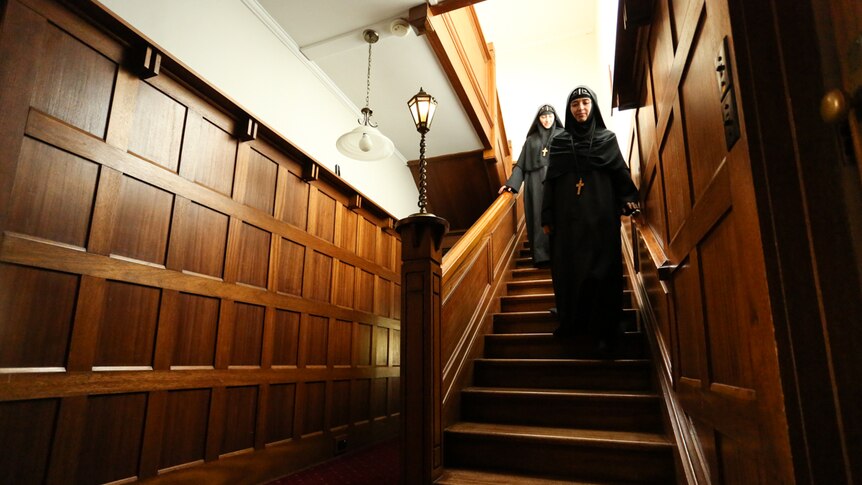 Two nuns walking down the wooden steps of the 1920s manor house which is now a monastery.