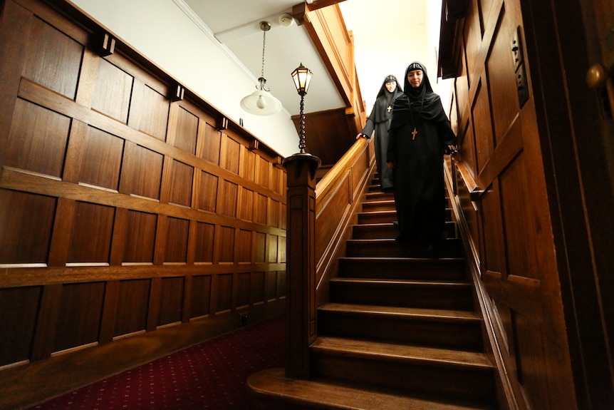 Two nuns walking down the wooden steps of the 1920s manor house which is now a monastery.