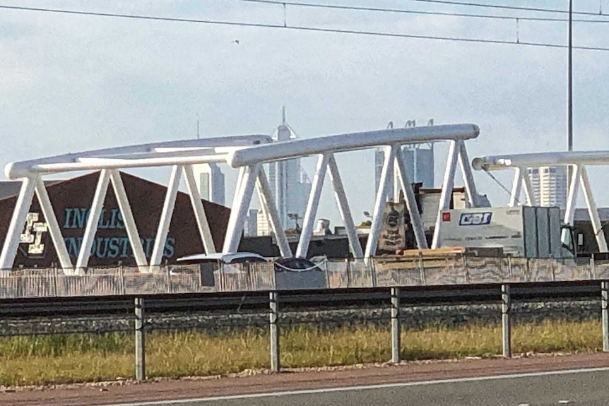 A truck carrying a large white bridge section on the freeway.
