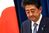 Shinzo Abe looks down as he speaks in front of a Japanese flag.