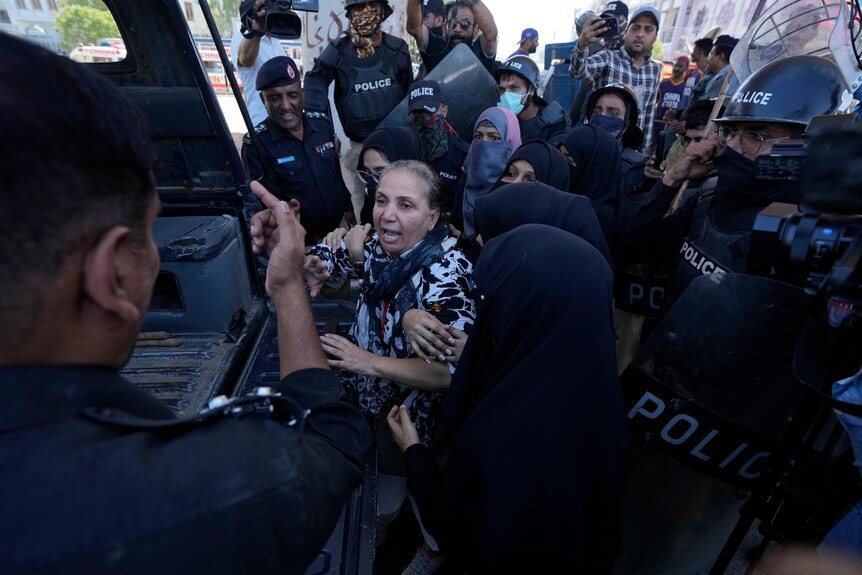 A Pakistani woman surrounded by police in riot gear leading her into van. 