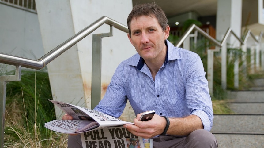 Kris Murphy sits on a set of stairs reading a newspaper