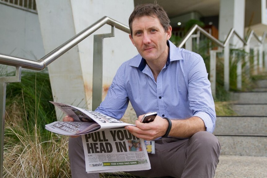 Kris Murphy sits on a set of stairs reading a newspaper