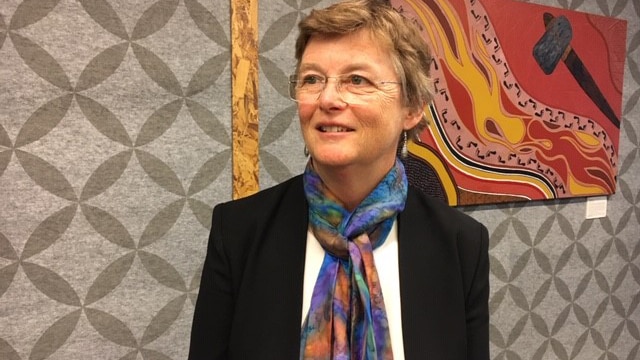 A mid shot of Medical Board of Australia chair Anne Tonkin posing for a photo standing in front of a painting on a wall.