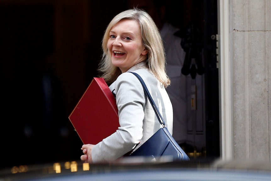 Liz Truss smiles and looks over her shoulder in front of the door of 10 Downing Street.