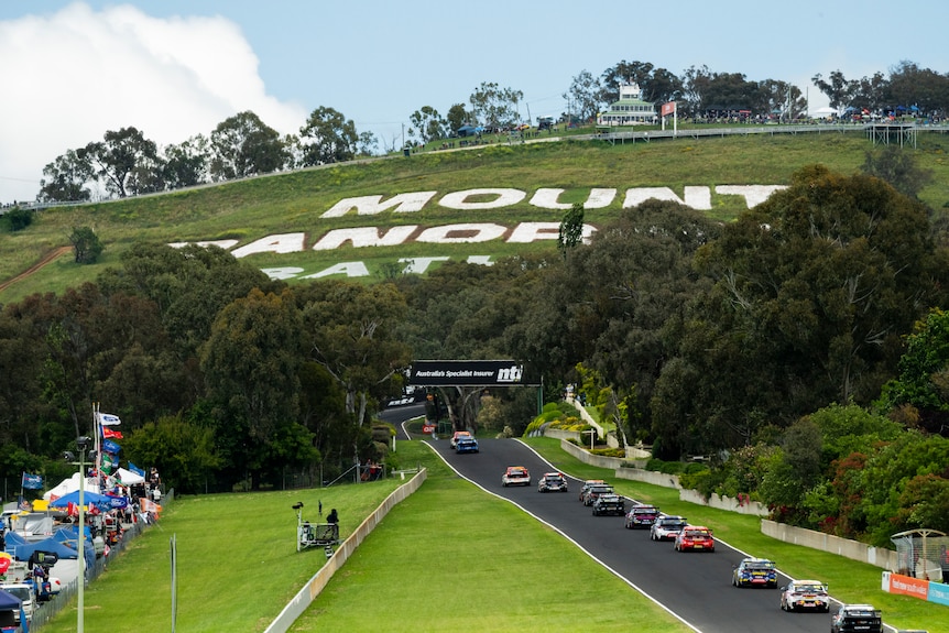Cars drive down a straight in front of the Mount Panorama sign at Bathurst