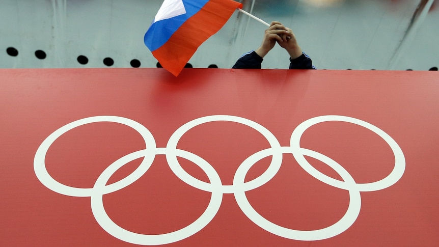 A Russian flag flies over a red advertising board with white Olympic rings depicted on it