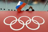 A Russian flag flies over a red advertising board with white Olympic rings depicted on it