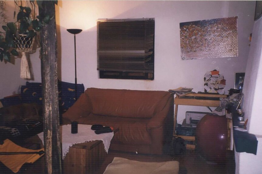 An interior of a house shows a couch, desks, a lamp, blinds, a table and a wall-mounted puzzle