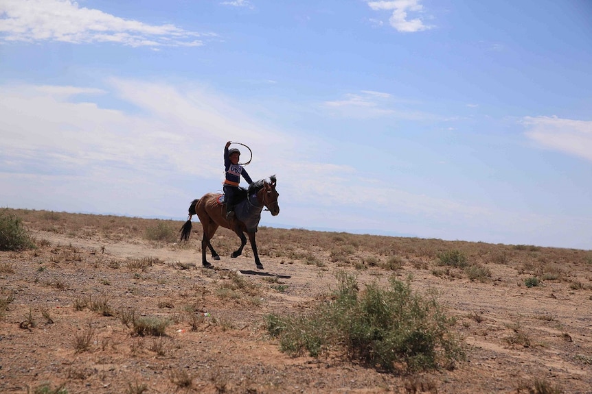 A young girl rides a horse and holds a whip in the Gobi Desert in Mongolia.