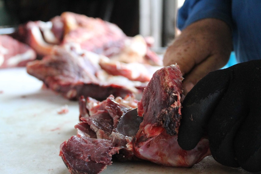 A hand with a knife easily slices through a large hunk of meat.