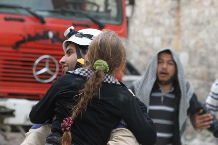 A man wearing a white helmet carries a young girl.