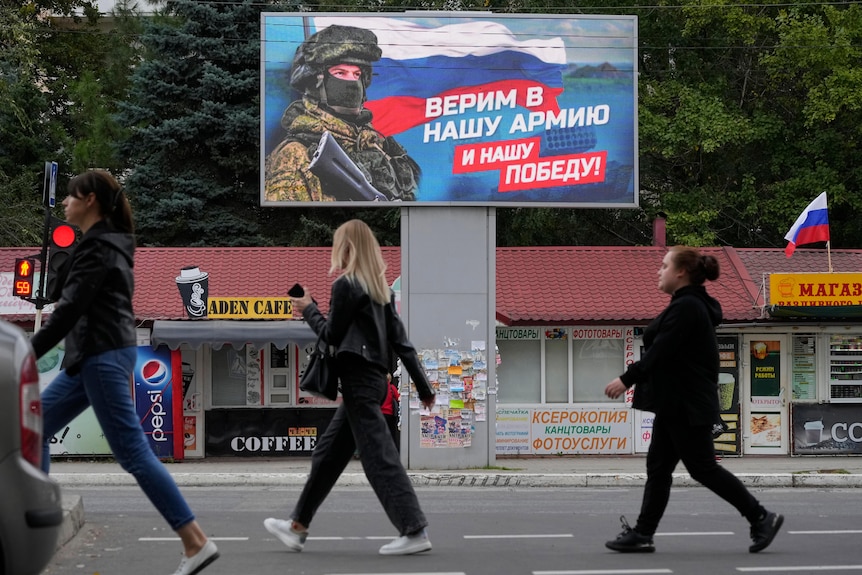 Les gens passent devant un panneau d'affichage affichant un soldat et un drapeau russe.