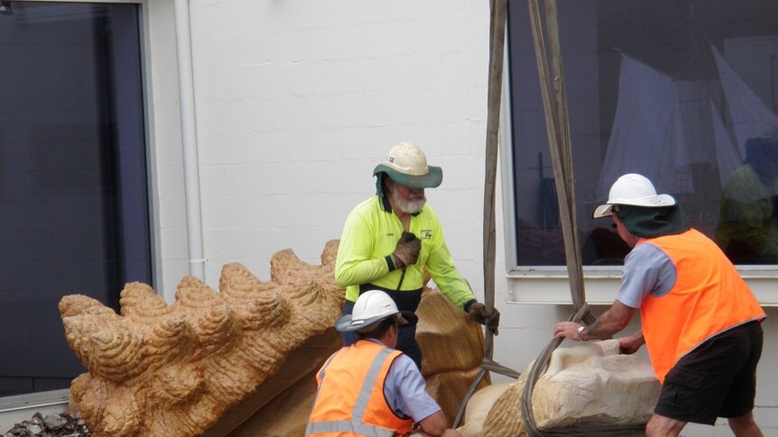 Workmen in hig-viz clothing remove a sculpture