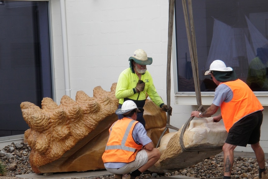Workmen in hig-vis work clothing remove a sculpture