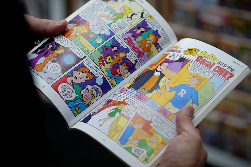 A man's hands holding a spread open page of the Archie comic book