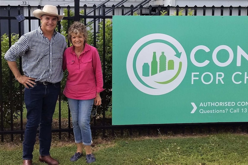 A man and woman stand next to a sign, smiling.