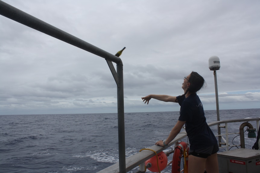 Oceanography student Hayley Rogers throws glass bottle over ship into the Pacific ocean