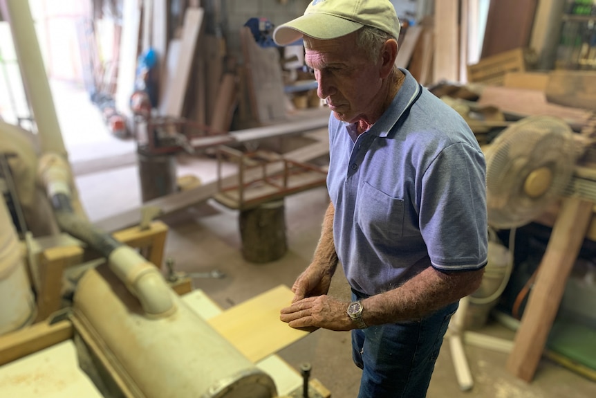 A man in a cap and blue shirt feeds a thin sheet of timber into a machine.