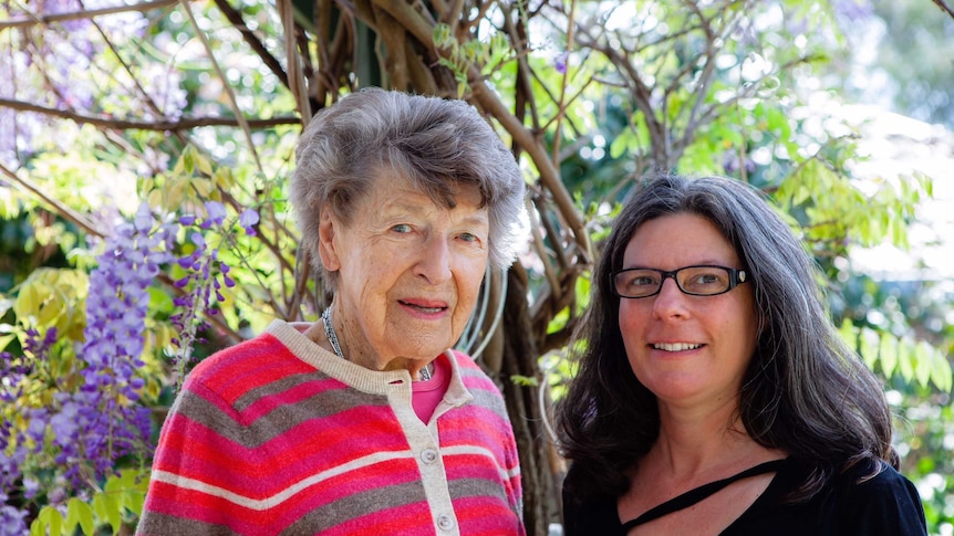 Joan, 94, and Yve, 52, standing in front of a wisteria plant