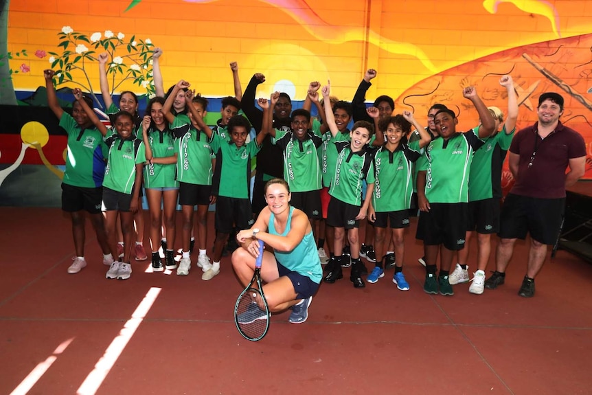 Ash Barty crouching down in front of group of students in green school uniforms