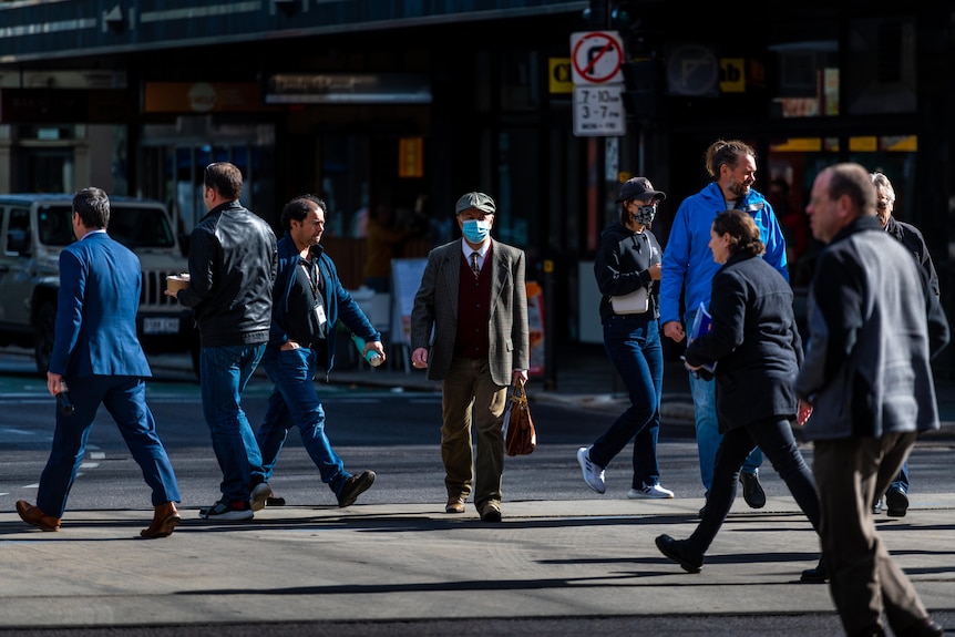 行人从各个不同方向穿过一条城市道路。一名走向镜头的男子戴着一个蓝色的外科口罩