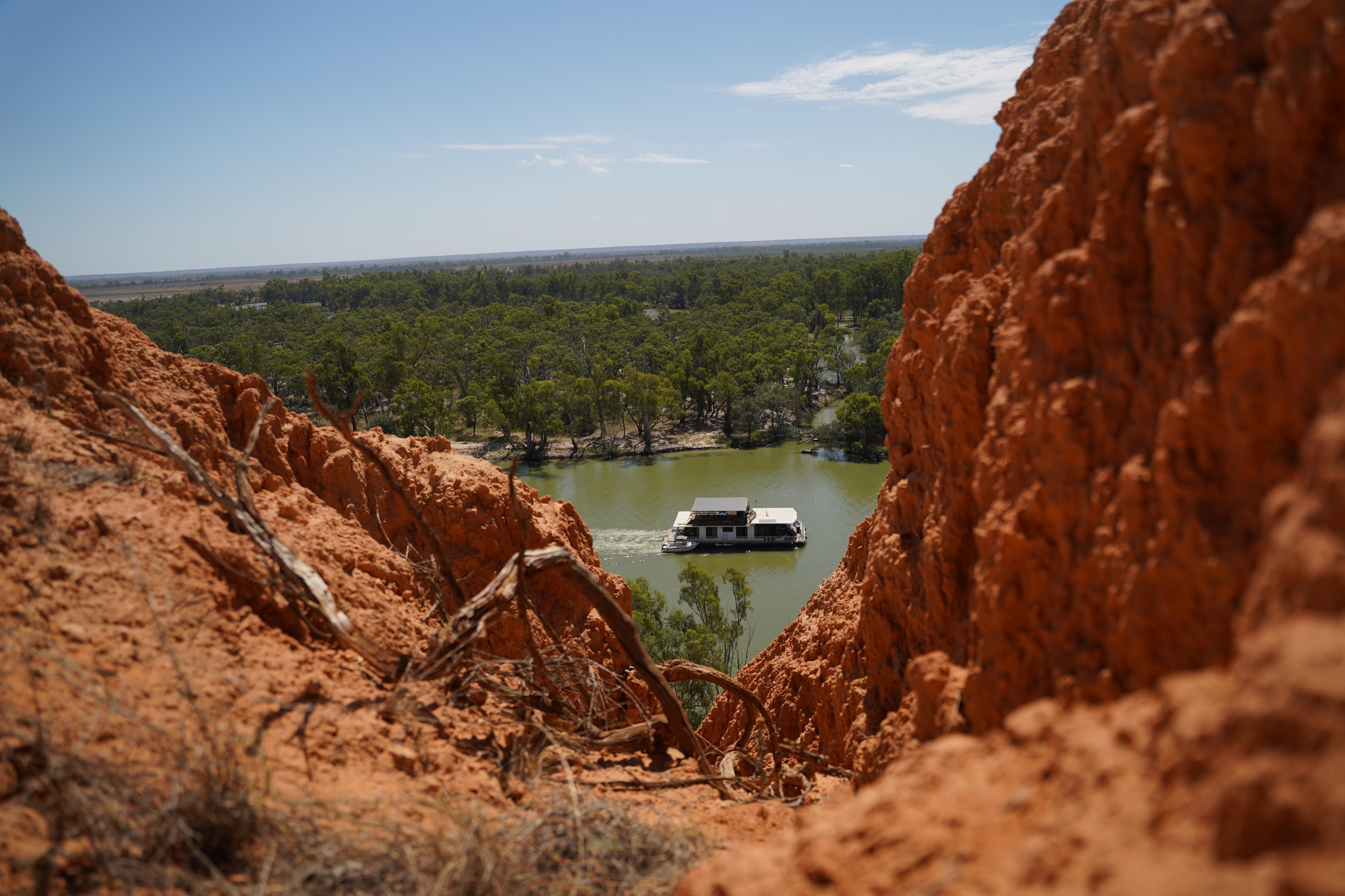 Una casa flotante flota río abajo por el río Murray. Se puede ver entre rocas secas y anaranjadas. 