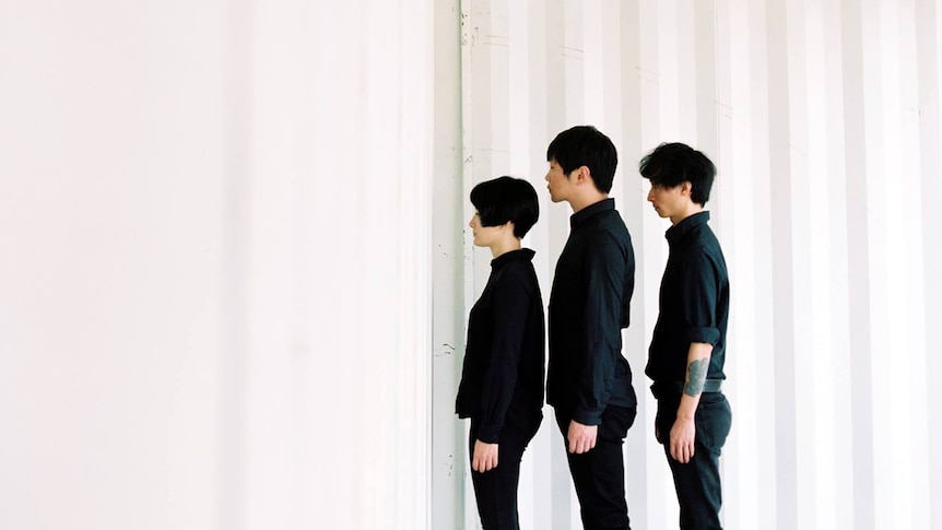 Three members of Chinese band Re-TROS stand in a completely white room staring at the wall, wearing black clothing