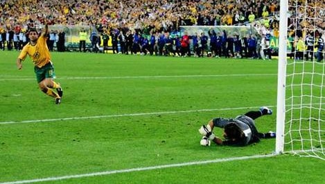 A soccer player celebrates after scoring a penalty shot. The goalie lays on the ground nearby.