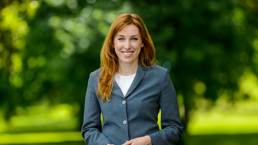 A woman standing in front of a green background. 