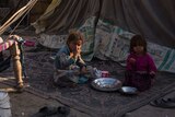 Two young Afghan girls eat on the ground in a run-down block of land.