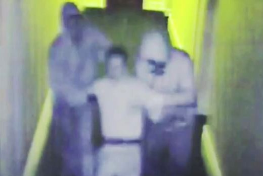 A still image taken from CCTV footage showing two men in hoodies marching another man along a corridor.