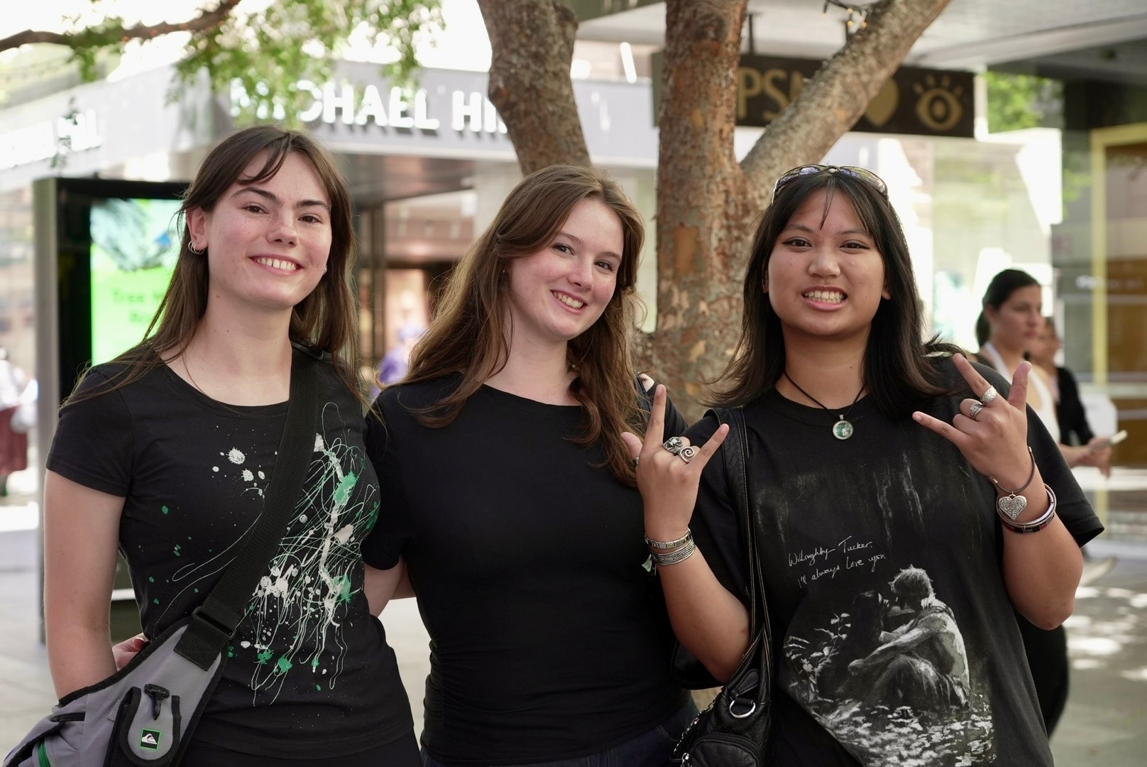 Three young women stand together, smiling.