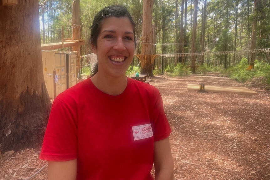 A woman stands in front of a ropes course.