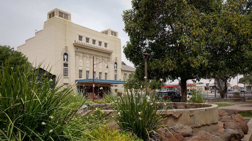 A facade of a traditional Australian town hall is seen among gardens.