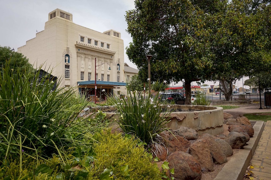 A facade of a traditional Australian town hall is seen among gardens.