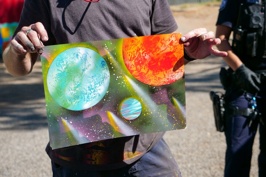 A man holds a piece of artwork of a solar system.