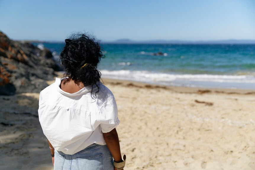 A woman wearing a white shirt looks out at the ocean.